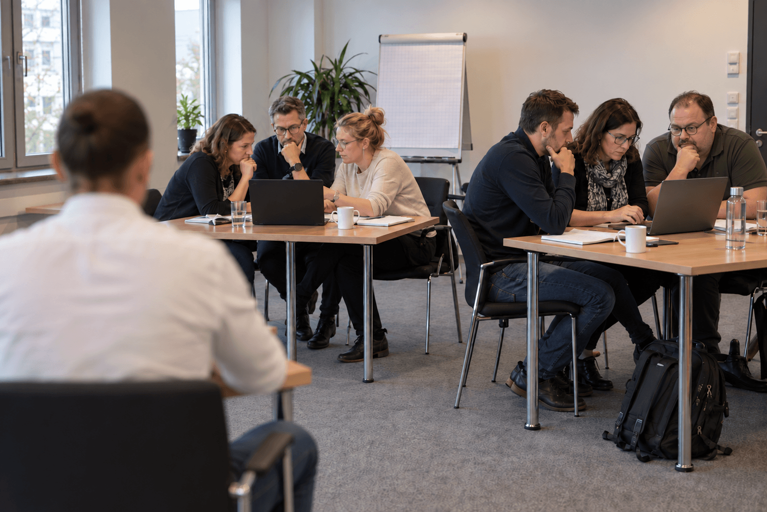 Teilnehmer arbeiten in kleinen Gruppen gemeinsam an Laptops in einem Workshop.